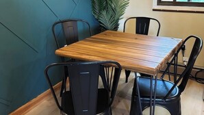 Un coin repas avec une table en bois et des chaises noires, une plante en pot et un tableau encadré au mur.