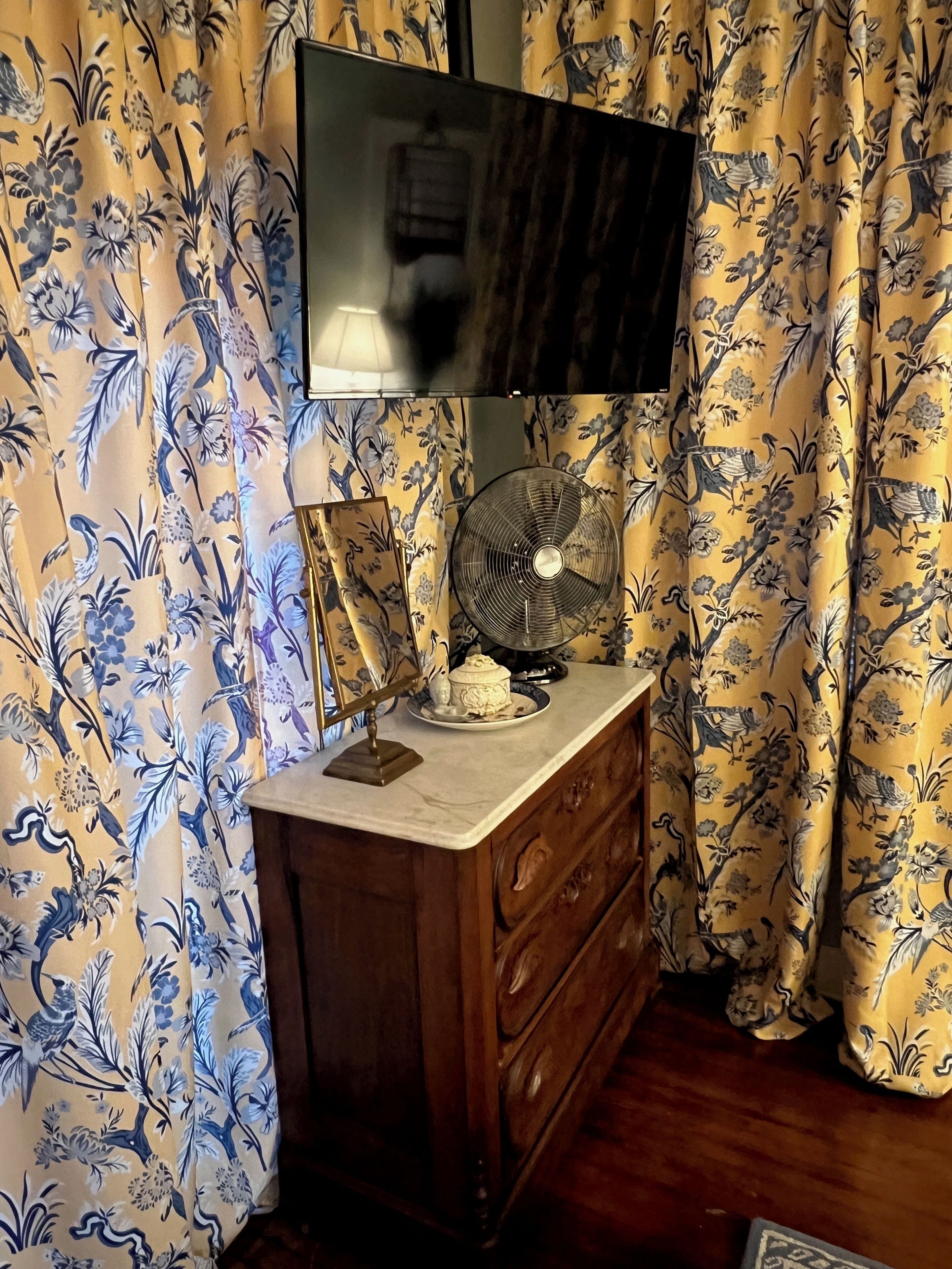 Quarto com cómoda de madeira, televisão de tela plana montada acima e um ventilador sobre a cómoda.