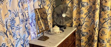 Quarto com cómoda de madeira, televisão de tela plana montada acima e um ventilador sobre a cómoda.