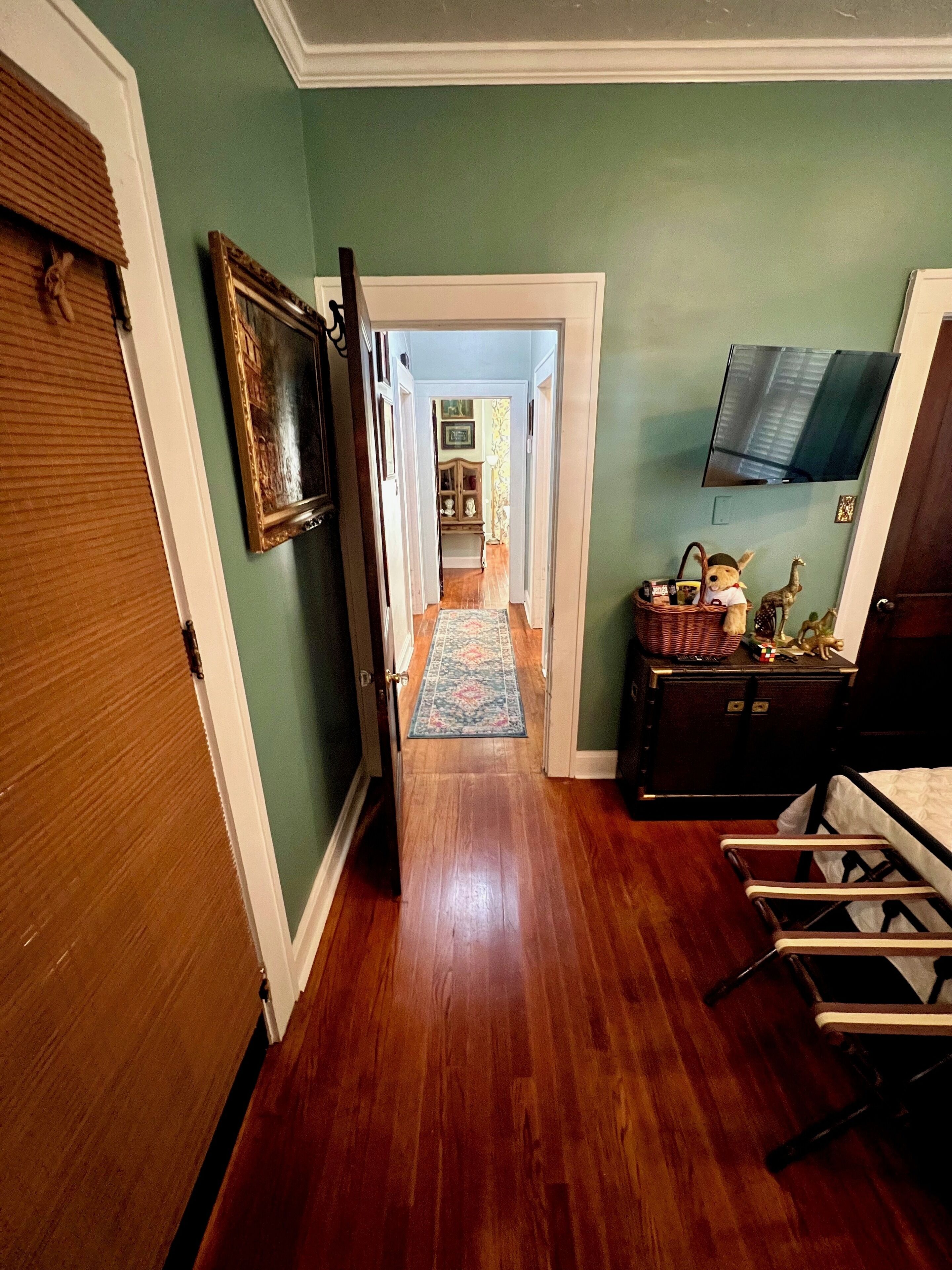 A hallway with wooden flooring, a television mounted on the wall, and a bed with a wooden frame.