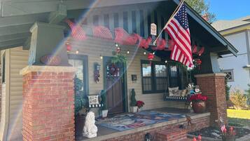 Una casa con porche decorado con una bandera estadounidense, un adorno navideño y un cartel que dice 'Merry Christmas'.
