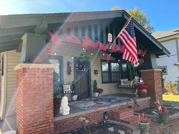 Una casa con porche decorado con una bandera estadounidense, un adorno navideño y un cartel que dice 'Merry Christmas'.