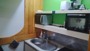 Una cocina compacta con un lavabo, microondas, tostadora y cafetera en una estantería.