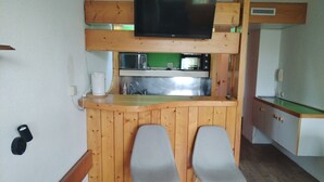 Una cocina compacta con encimera de madera, dos taburetes grises, un microondas y un televisor montado sobre la encimera.
