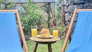 Una mesa con un croissant y dos vasos de jugo de naranja, ubicada entre dos sillones azules, con montañas al fondo.