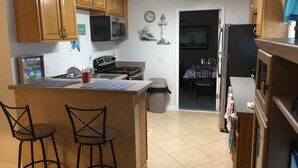 A kitchen with wooden cabinets, a microwave, a stove, and a refrigerator. There are two bar stools and a trash can. A clock and a decorative item are on the wall. - 3-bedroom house in marvelous Hudson with AC, WiFi (Hudson)