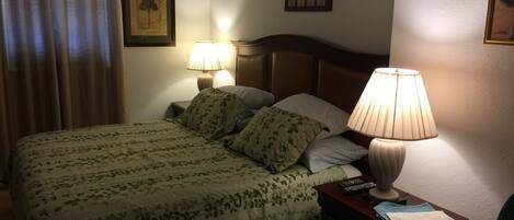 A neatly made bed with floral bedding, two bedside lamps, a ceiling fan, and a small table with a remote control.