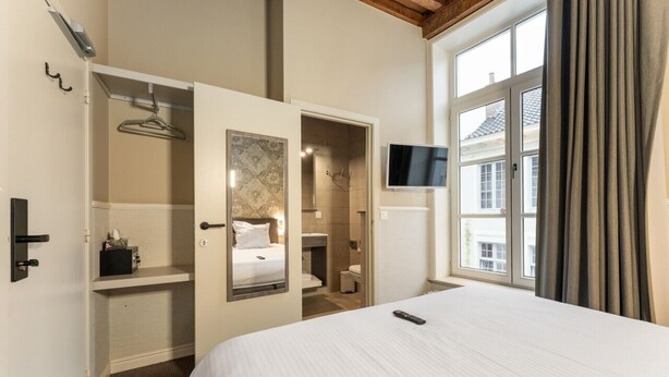 Habitación de hotel con cama, televisión, armario y baño visible a través de una puerta abierta.