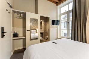 Habitación de hotel con cama, televisión, armario y baño visible a través de una puerta abierta.