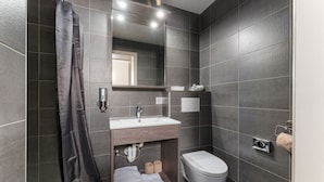 Une salle de bain moderne avec des carreaux de couleur sombre, un lavabo blanc, des toilettes et un rideau de douche.