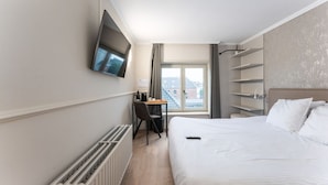 Une chambre d’hôtel équipée d’un lit, d’un bureau, d’une chaise, d’un téléviseur fixé au mur et d’une fenêtre avec des rideaux.
