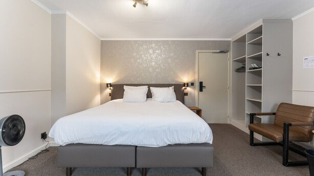 A bedroom with a bed, bedside lamps, a fan, a chair, and a wardrobe. - Contemporary Room in Bruges' Heart (Brugge)