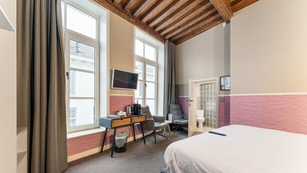 A hotel room with a bed, desk, chair, TV, and large windows. - Hotel Karel de Stoute (Brugge)