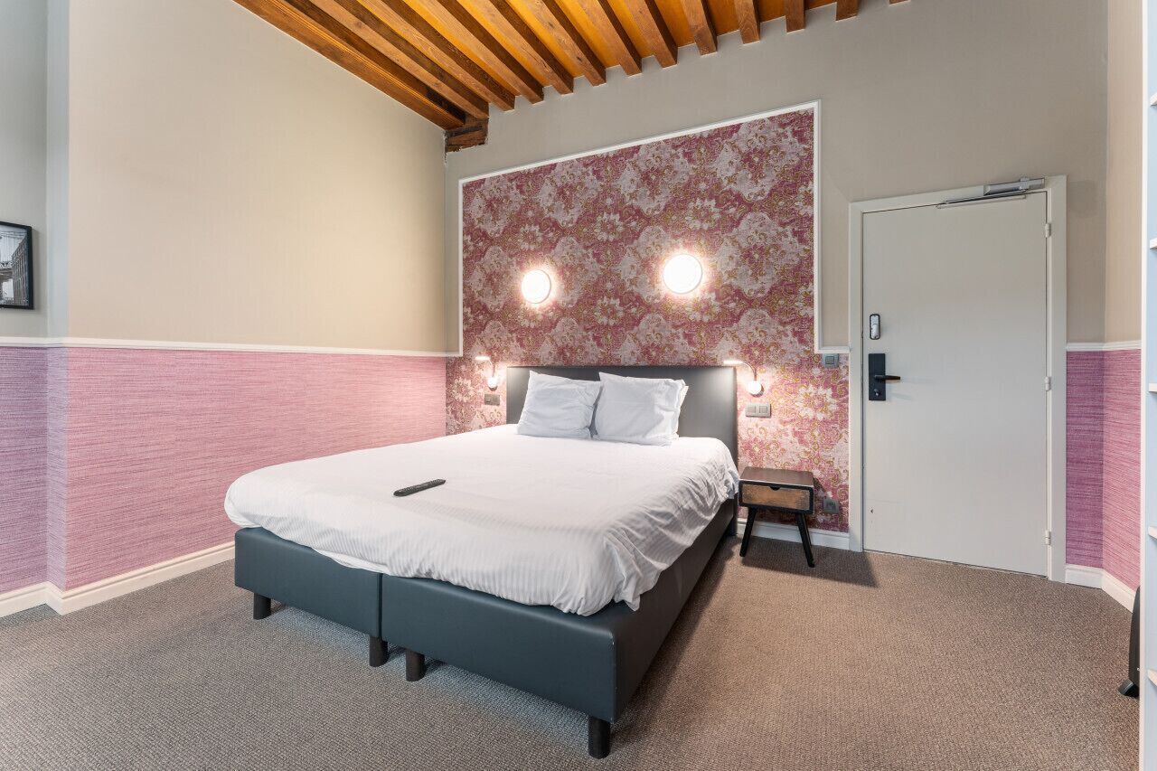 Ein modernes Hotelzimmer mit einem großen Bett, einer Holzbalkendecke und einem gemusterten Wandteppich.