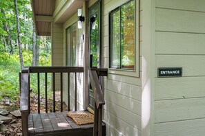 A wooden porch with a bench and a rug, leading to a building with a sign reading 'ENTRANCE'. - Serenity Cabin-Woodland Retreat (Wintergreen Resort)