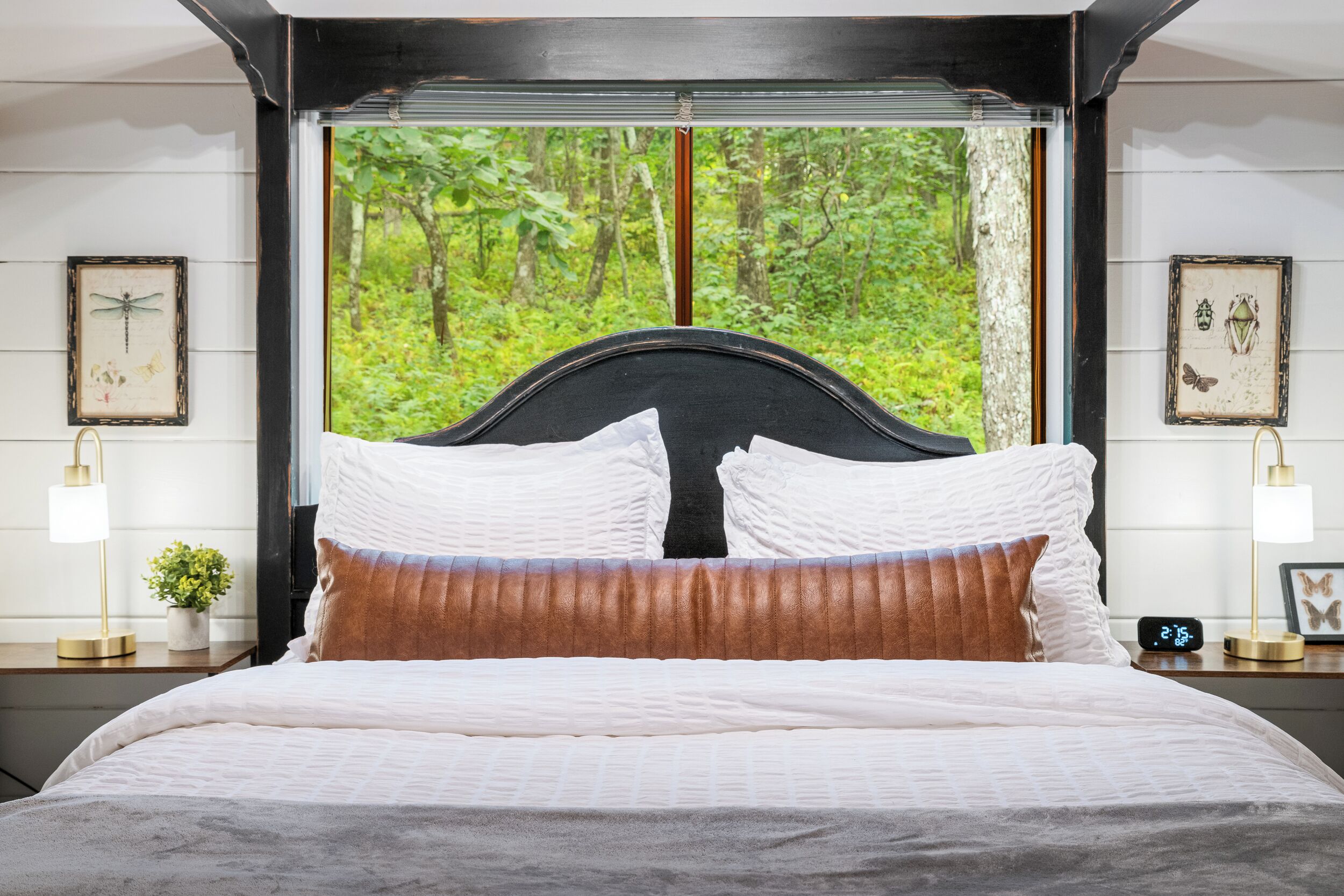 A bedroom with a large window, a bed with white bedding, a headboard, and two bedside tables with lamps.
