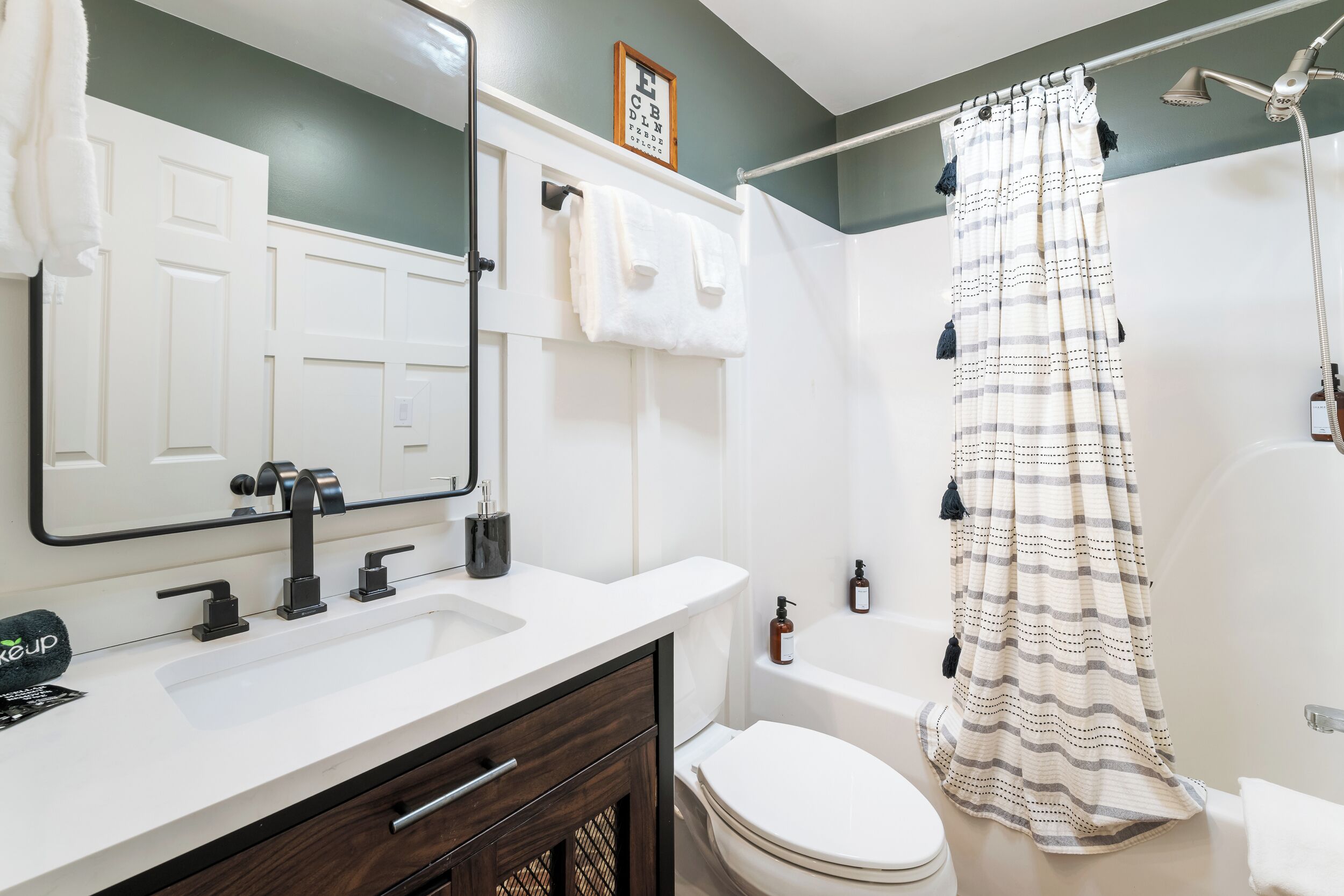 Un bagno con un lavandino bianco, un mobile contenitore in legno scuro, un water bianco e una doccia con tenda a righe.