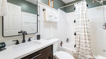 Un bagno con un lavandino bianco, un mobile contenitore in legno scuro, un water bianco e una doccia con tenda a righe.