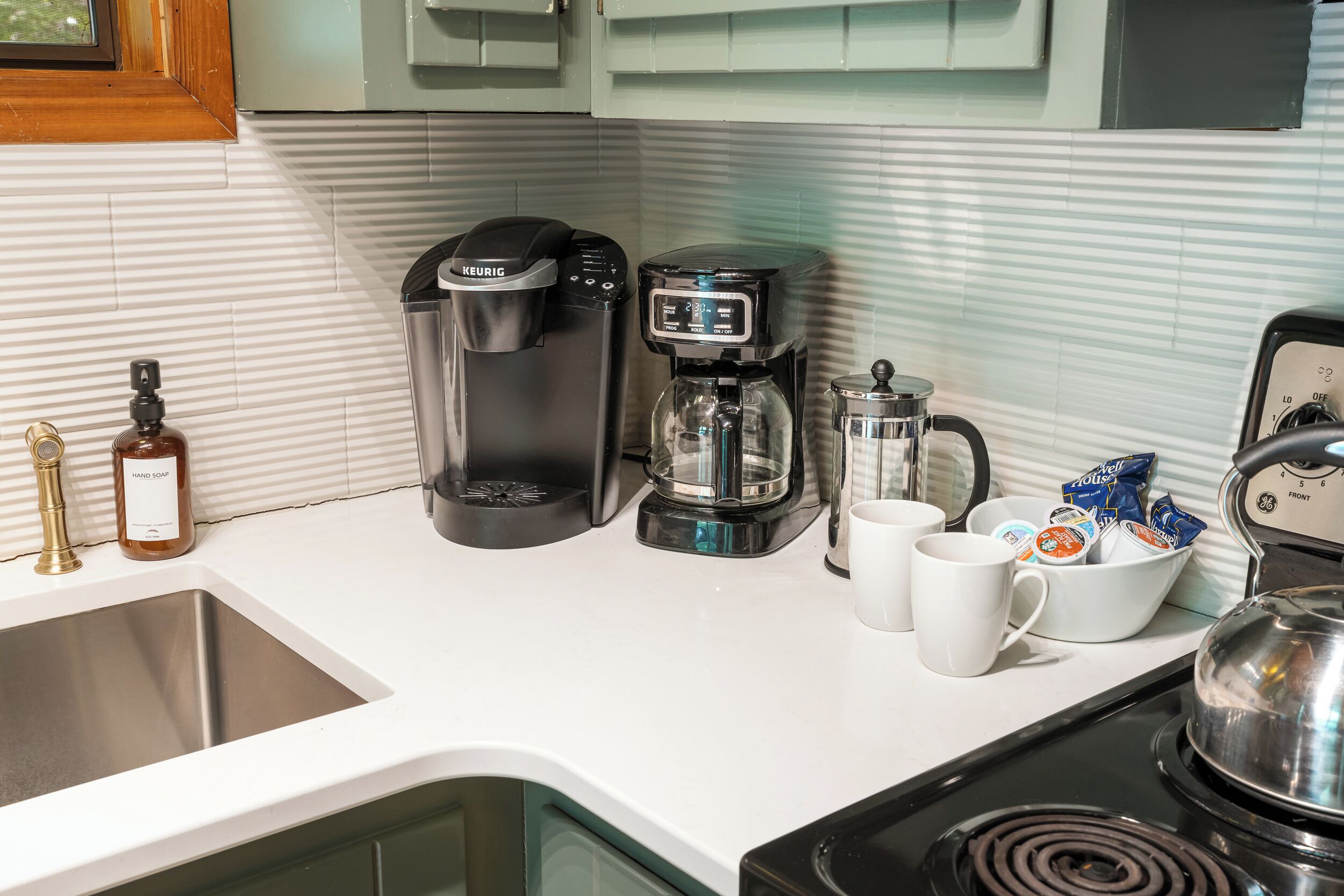 Une cuisine équipée d’une machine à café, d’une bouilloire, d’une cafetière et d’une tasse.