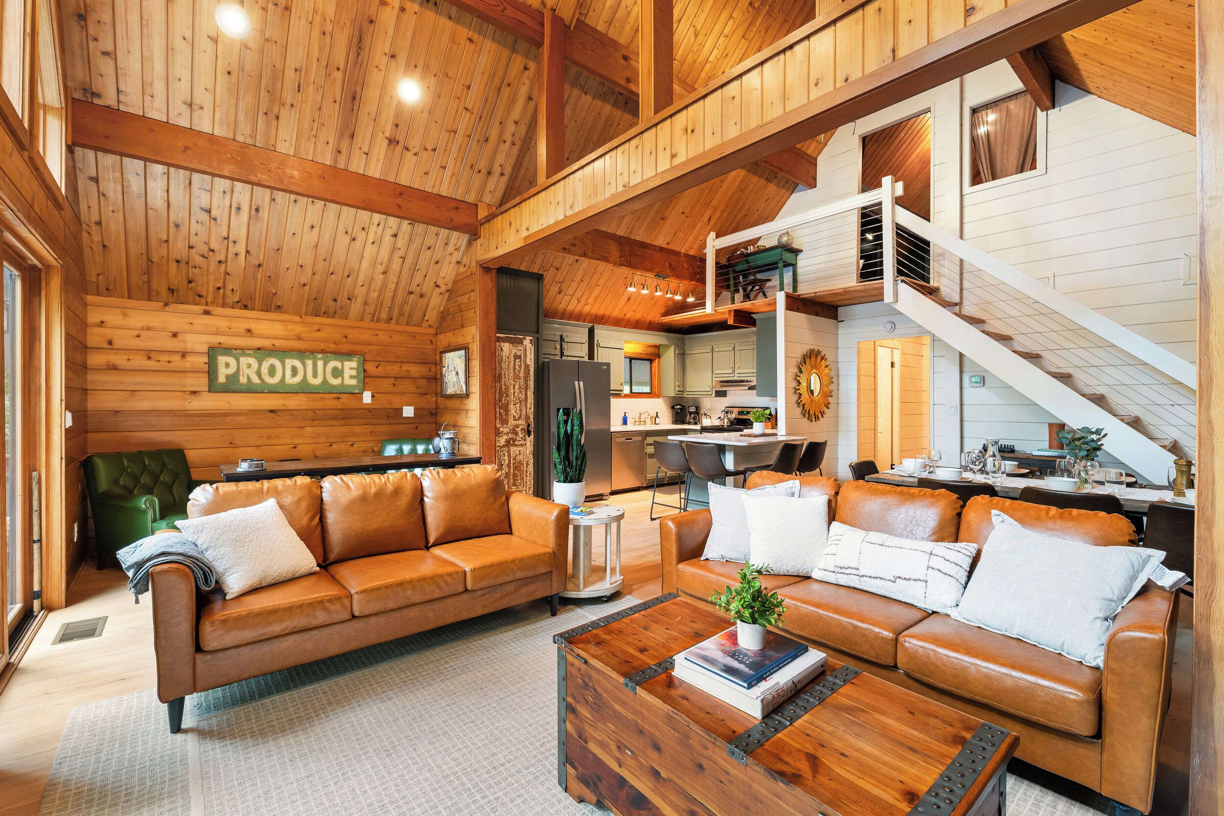 A spacious living area with a wooden ceiling, a sofa set, a coffee table, and a kitchen in the background.