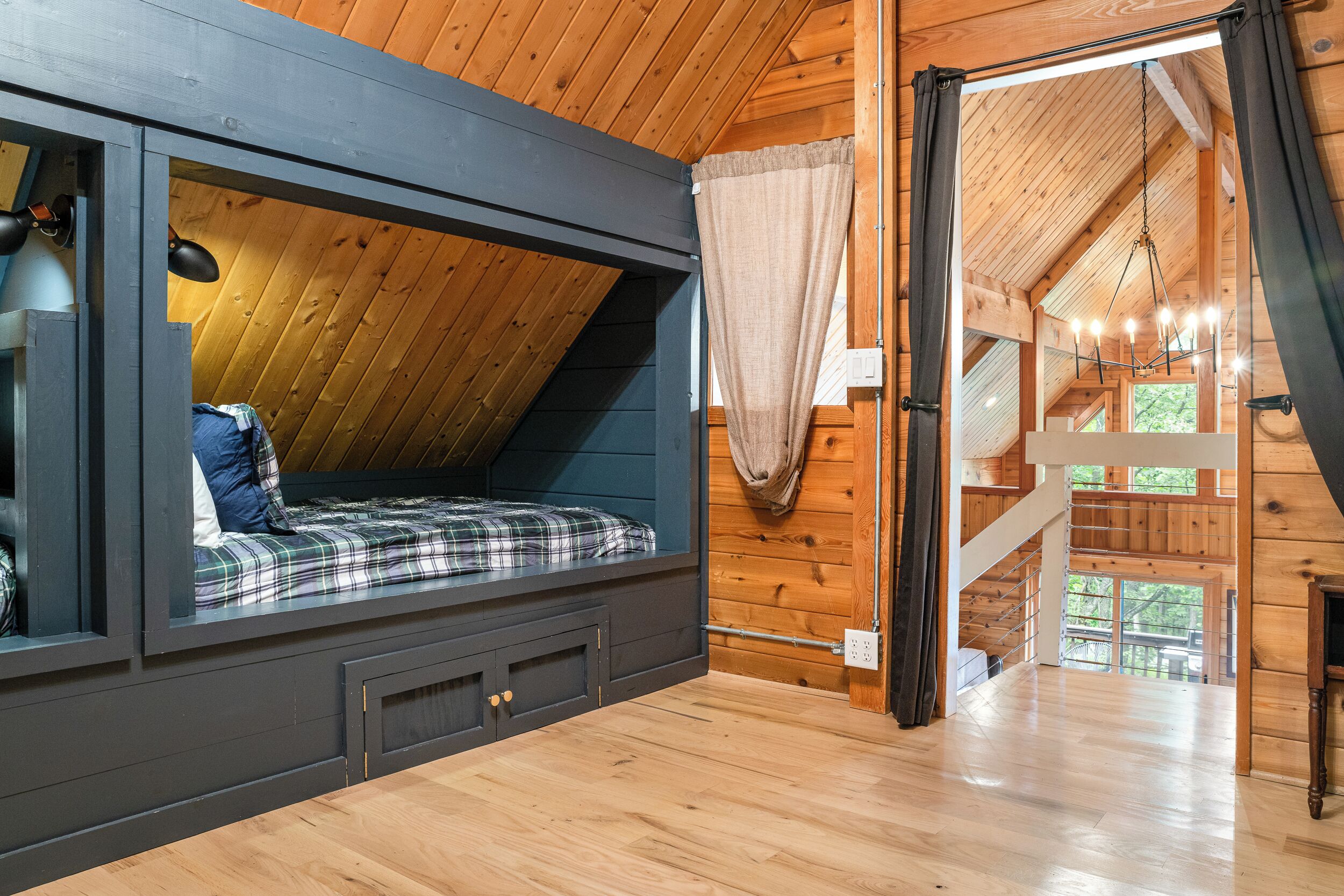 Una camera mansardata con soffitto spiovente, un letto con copriletto a quadri, una cassettiera scura e vista sull'esterno attraverso una finestra.