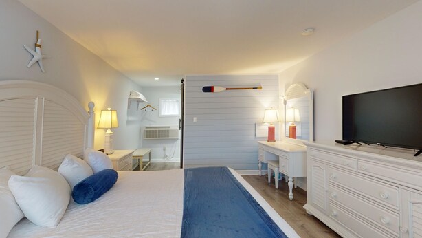 A bedroom with a bed, bedside tables, a dresser, a television, and a desk with a chair. - Spacious King Room for a Serene Getaway (Cape May)