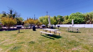 An outdoor area with picnic tables and umbrellas, surrounded by trees and a fence. - Spacious King Room for a Serene Getaway (Cape May)