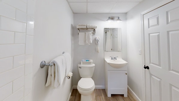 A small, clean bathroom with white tiles, a toilet, a sink, and a towel rack.