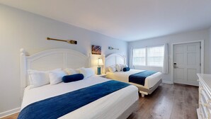Et hotelværelse med to senge, et natbord med lampe, et maleri og et vindue med gardiner.