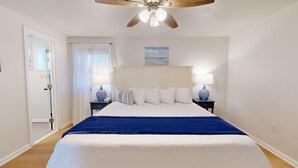 A bedroom with a large bed, two bedside tables with lamps, a ceiling fan, and a window with curtains. - Two-Bedroom Suite for the Ultimate Family Vacation (Cape May)