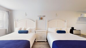 A hotel room with two beds, a nightstand, a small table, and a wall-mounted heater. - Double Queen Room for a Cozy Group Stay (Cape May)