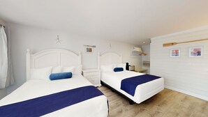 A hotel room with two beds, a small bedside table, a nightstand, and a wall-mounted shelf with towels. - Double Queen Room for a Cozy Group Stay (Cape May)
