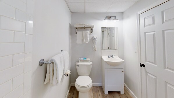 Bany petit i net amb rajoles blanques, vàter, un lavabo i una barra per a tovalloles.