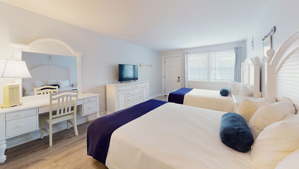 Une chambre d’hôtel avec deux lits, un bureau avec une chaise, une télévision et une armoire.