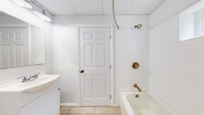 A bathroom with a white sink, mirror, and bathtub. - Luxury and Space in a Double King Room (Cape May)