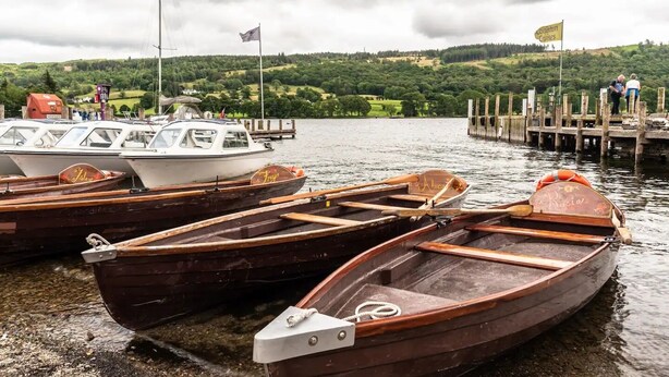 Several wooden rowboats docked at a pier with a backdrop of green hills and a cloudy sky. - Beautiful Detached Farm House Near Lake Coniston - Pass the Keys (Torver)