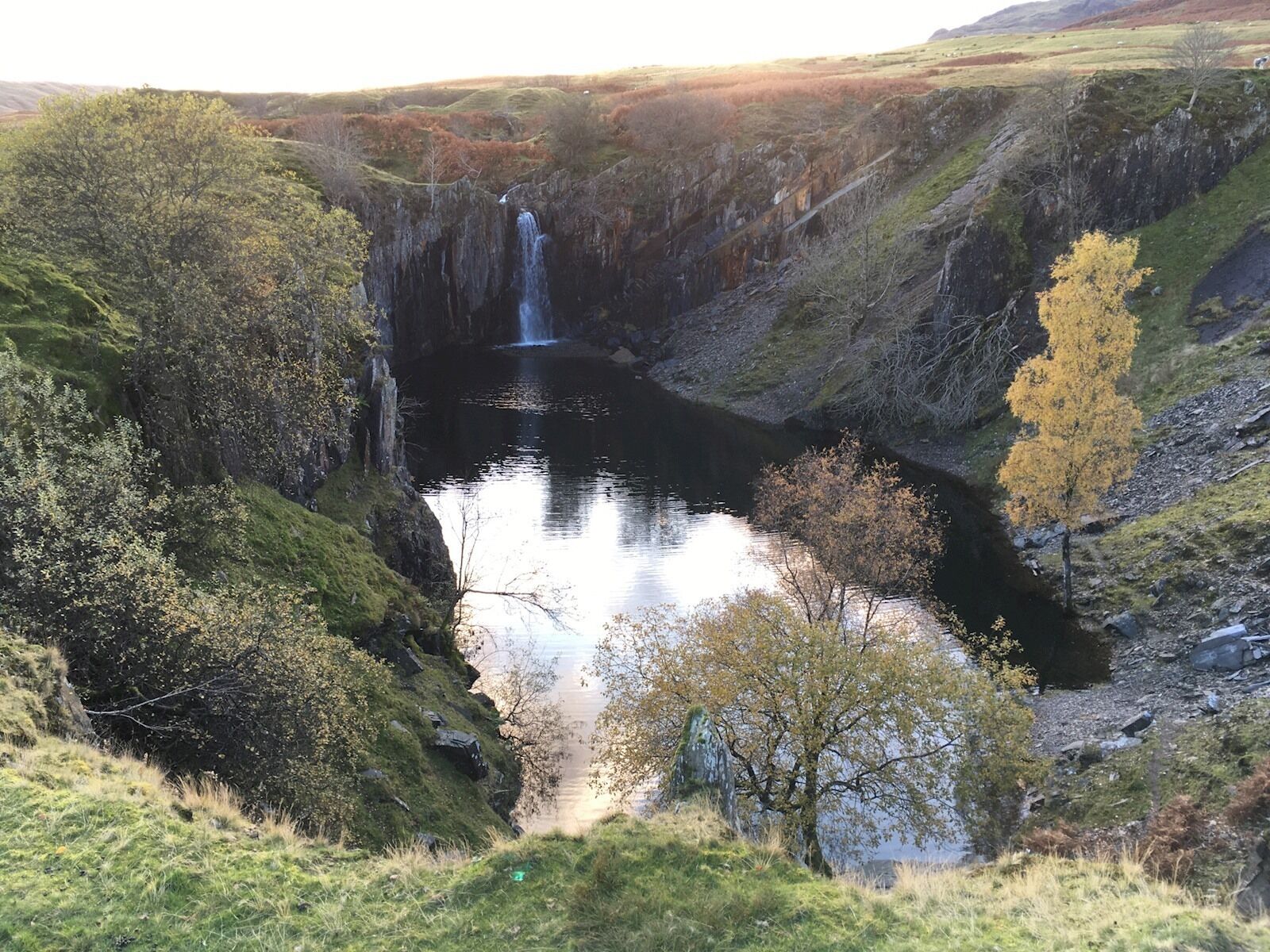 Ett vattenfall i en dal omgiven av träd och kullar.