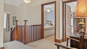 A hallway with a wooden railing, a carpeted floor, a table with a lamp, and a mirror. - Beautiful Detached Farm House Near Lake Coniston - Pass the Keys (Torver)