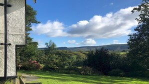 A grassy lawn with a wooden bench and a white building with a black roof. - Beautiful Detached Farm House Near Lake Coniston - Pass the Keys (Torver)