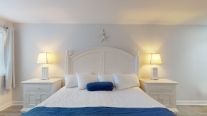 A bedroom with a large bed, white headboard, two bedside tables with lamps, and a star decoration on the wall. - Elegant King Room for a Relaxing Beach Escape (Cape May)