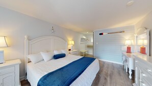 A neatly arranged bedroom with a bed, bedside tables, a dresser, and a wall-mounted mirror. - Elegant King Room for a Relaxing Beach Escape (Cape May)