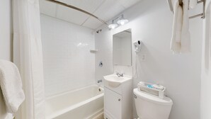 A modern bathroom with a white bathtub, a sink, and a toilet. - Elegant King Room for a Relaxing Beach Escape (Cape May)