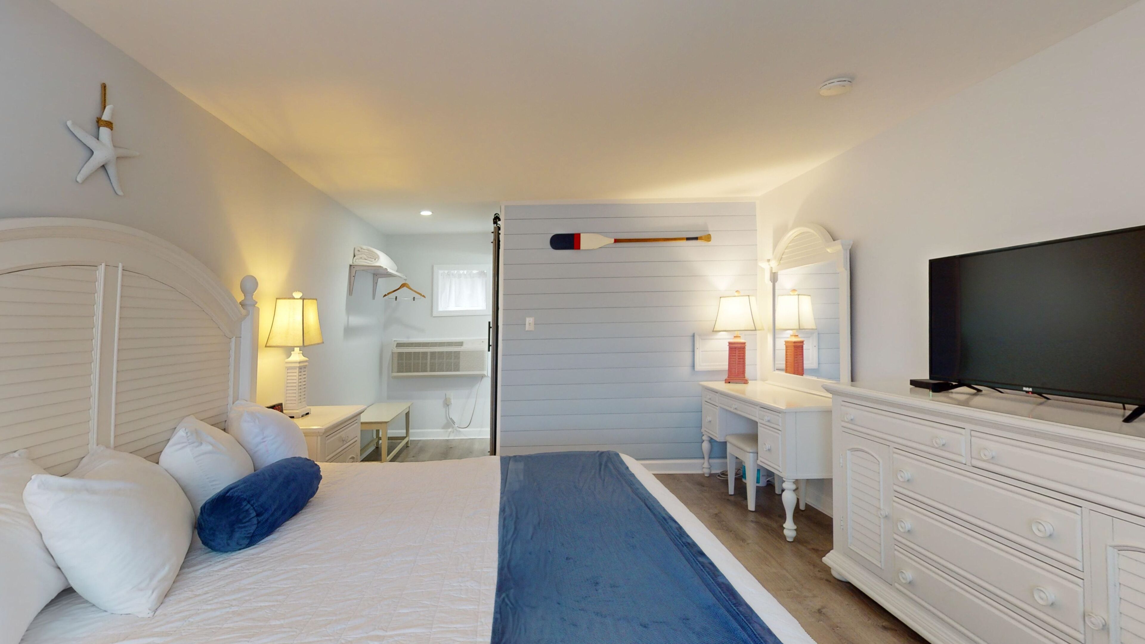 A bedroom with a bed, bedside tables, a dresser, a television, and a desk with a chair.