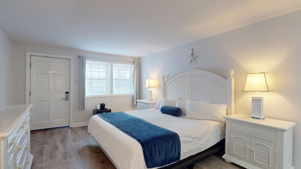 Een slaapkamer met een bed, twee nachtkastjes met lampen, een dressoir, een raam met gordijnen en een deur.