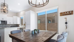 A modern kitchen with white cabinets, a wooden dining table, and a view of a backyard through glass doors. - Mountain Top Oasis with lake views  - WiFi included (Lake Havasu City)