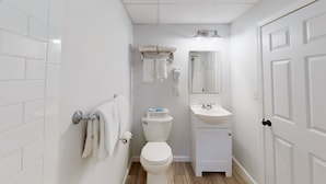 A small, clean bathroom with white tiles, a toilet, a sink, and a towel rack.