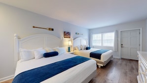 A hotel room with two beds, a nightstand with a lamp, a painting, and a window with curtains.