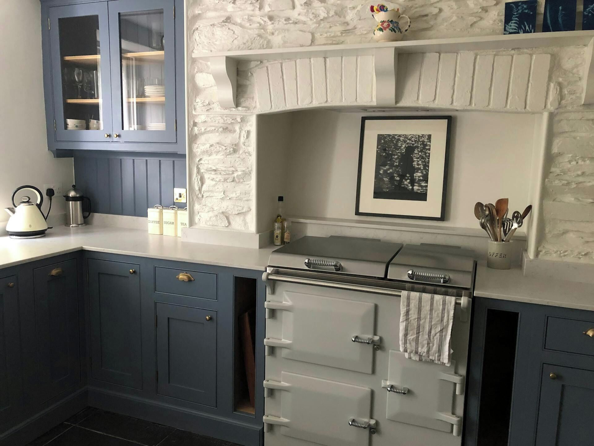 A kitchen with blue cabinets, a white stove, and a stone wall.