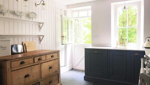 Eine Küche mit weißen Wandverkleidungen, einem Holzschrank, einem blauen Schrank und einem Fenster mit Blick auf Grünflächen.