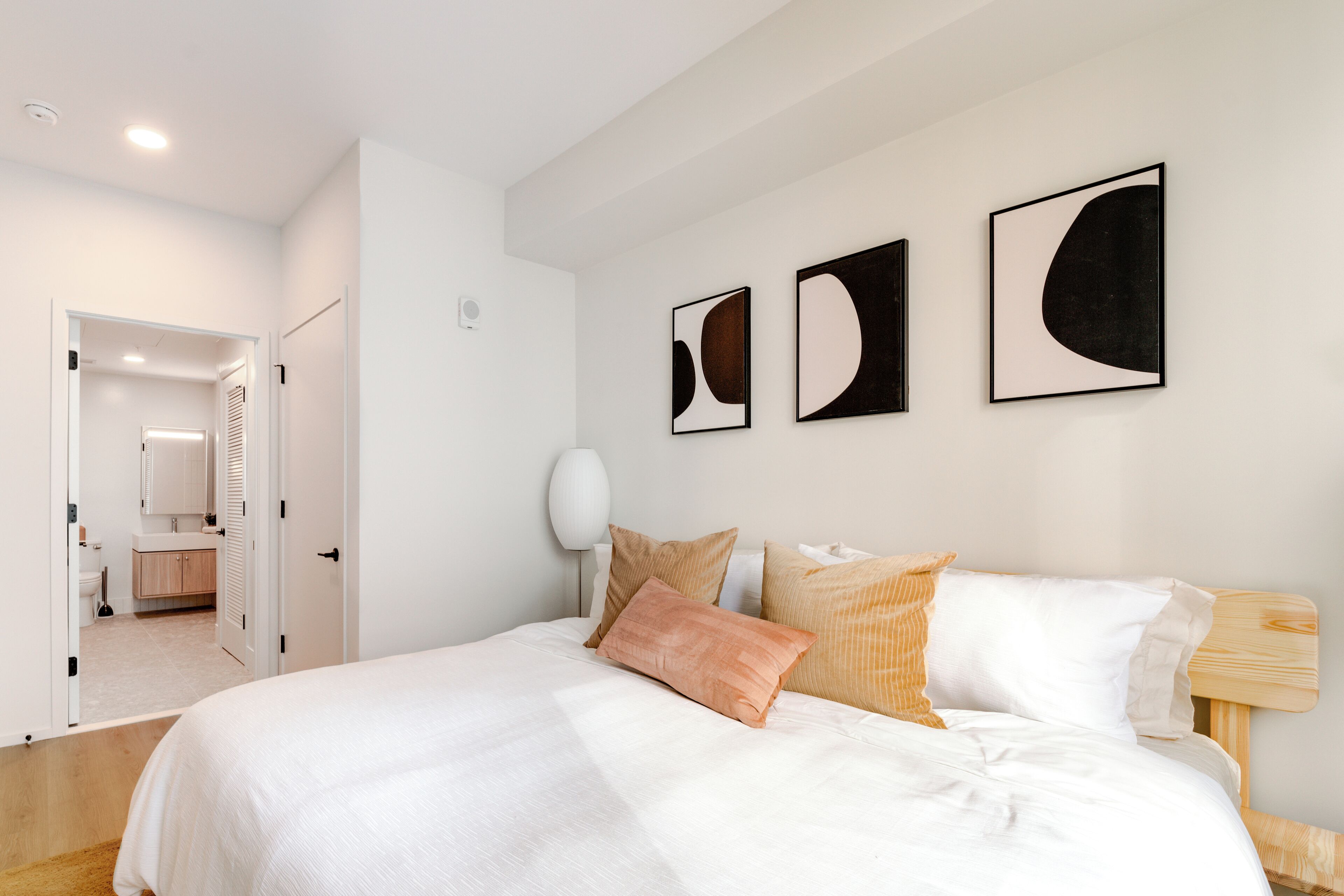 Ein modernes Schlafzimmer mit einem großen Bett, weißer Bettwäsche und drei abstrakten Wandbildern.